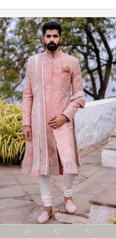 a man in a pink sherwa with white pants and shoes standing on steps