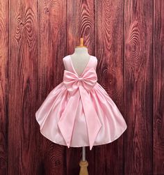 Our enchanting Knee Length flower girl dresses are sure to turn heads! This beautiful elegant sophisticated dress is handmade, the bodice consists of Pink Bridal Satin with a sowed in sash at the waist, the back of the dress consists of an open V-back with a zipper. The big bow is detachable. The skirt consists of pink satin followed by lining and crinoline for a fuller look. Extremely light weight and beautiful. This dress is perfect for any occasion!  Dress Is Pictured with a petticoat NOT INC Elegant Pink Princess Dress For Pageants, Elegant Pink Princess Dress For Pageant, Princess Style Pageant Dress With Satin Bow, Elegant Princess Wedding Dress With Bow Tie Back, Elegant Wedding Princess Dress With Bow Tie Back, Princess Style Baptism Dress With Bow, Fitted Princess Dress With Satin Bow For Bridesmaids, Princess Satin Bridesmaid Dress, Satin Princess Bridesmaid Dress