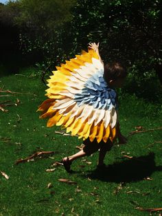 a young boy is playing with a large paper bird on the grass in front of some trees