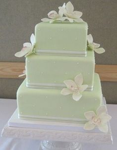 a three tiered green cake with white flowers on the top and bottom, sitting on a table