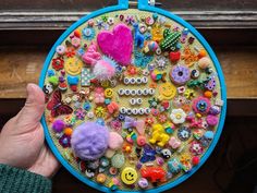 a person holding up a colorful piece of art made out of buttons and other things