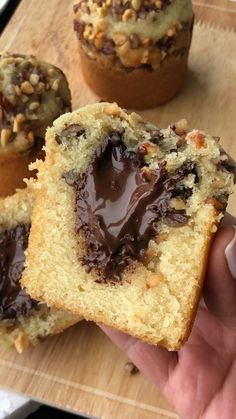 a person holding a chocolate filled muffin in their hand with other muffins behind them