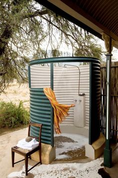 an outdoor shower in the middle of a dirt area with a chair next to it