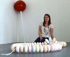 a woman sitting on the floor next to a large pipe with colored yarn all over it