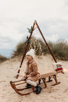 Little girl sitting on a vintage sleigh on the beach with a triangle arch in the background. Christmas Mini Photoshoot, Christmas Mini Sessions Outdoor, Photoshoot At The Beach, Christmas Mini Shoot, Mini Photoshoot, Christmas Family Photoshoot