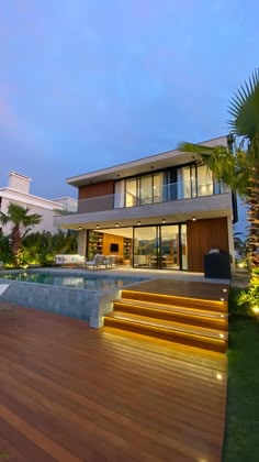 a modern house with wooden steps leading to the pool and deck area at night time