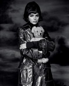 a black and white photo of a woman in a trench coat holding a teddy bear