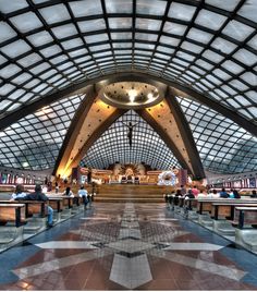 the inside of a train station with many people walking around and sitting on benches in front of it