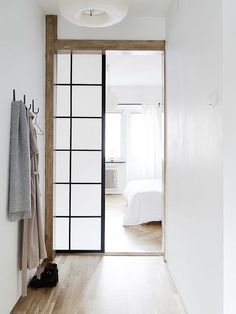 an open door leading to a bedroom with white walls and wood floors, along with clothes hanging on hooks