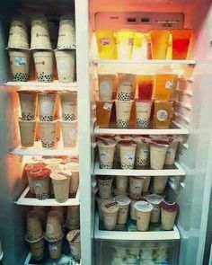 an open refrigerator filled with lots of cups and drinks on it's shelves in front of the door