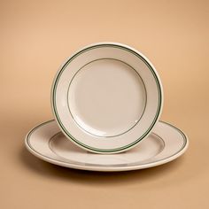 two white plates with green trim sit on a tan surface, one has a fork and knife in it