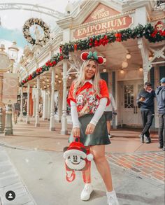 a woman standing in front of a building holding a skateboard wearing mickey mouse ears