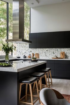 a kitchen with black cabinets and stools next to an island countertop that has plants on it