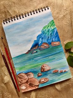 a watercolor painting of rocks and mountains on a table next to a plant with two pencils