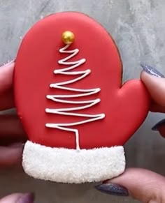 someone is holding a decorated cookie in the shape of a heart with a christmas tree on it