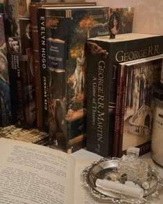 several books are sitting on a table next to an open book and glass ashtray