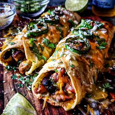 several burritos on a wooden cutting board with lime wedges and salsa in the background