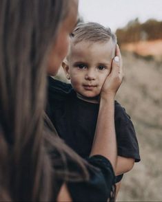 a woman holding a little boy in her arms while he looks at the other side