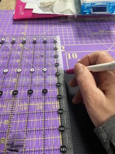 a person is cutting out small black circles on a purple mat with a white marker