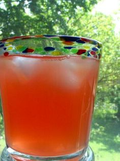 a close up of a drink in a glass on a window sill with trees in the background