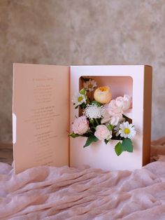 an open card with flowers in it on a bed