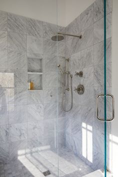 a walk in shower sitting next to a white tiled wall with glass doors and shelves