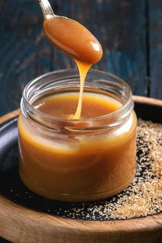 a spoon full of caramel sauce being poured into a jar