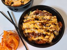 two black bowls filled with food and chopsticks next to each other on a white table