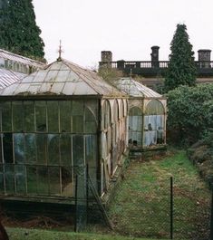 an old greenhouse in the middle of a grassy area with lots of trees and bushes around it