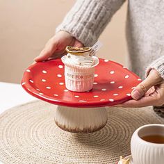 a woman is holding a red plate with a cupcake on it and a spoon in her hand