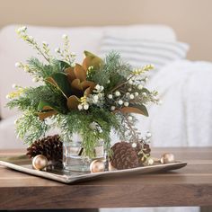 a glass vase filled with greenery on top of a table next to pine cones