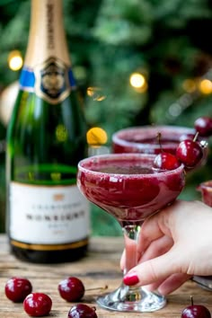 a person holding a wine glass with cherries on it and a bottle in the background