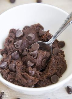 a bowl filled with chocolate ice cream on top of a wooden table next to chocolate chips