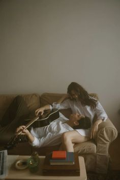 a man and woman sitting on a couch playing the guitar in front of a coffee table