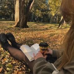 a woman sitting on the ground holding a cup of coffee and looking at her book