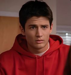 a young man in a red hoodie looking at the camera with an intense look on his face