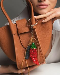 a woman holding a brown purse with a red and green beaded keychain