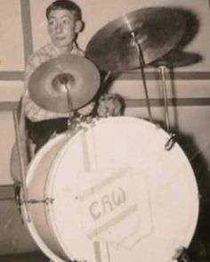 an old photo of a man playing drums in front of a wall with the word crw on it