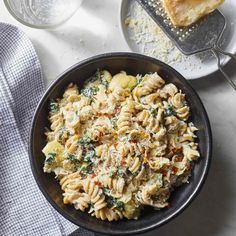 a bowl filled with pasta and spinach on top of a table next to bread