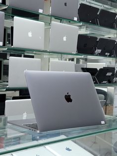 an apple laptop sitting on top of a glass table next to other macbook computers