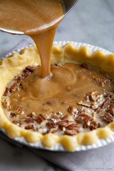 someone pouring caramel sauce on top of a pecan tart crust in a pie pan