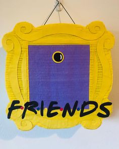 a yellow frame with the word friends written on it hanging from a hook in front of a white wall