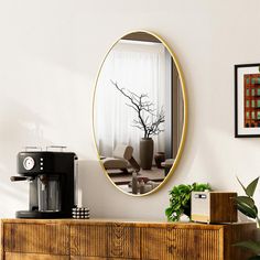 a round mirror hangs on the wall above a dresser and coffee maker in a living room