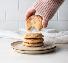 a person holding a cookie in their hand over a stack of cookies on a plate