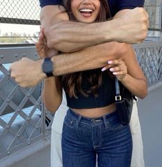 two people hugging each other while standing on a bridge with their arms around one another