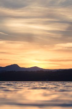 the sun is setting over water with mountains in the background