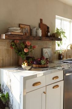 a kitchen with white cabinets and marble counter tops, gold pulls on the cabinet doors