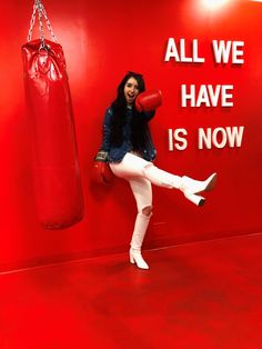 a woman posing in front of a red wall with boxing gloves hanging from it's hooks