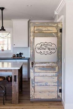 an old door is opened to reveal a kitchen with white cabinets and wood floors, along with a bar stools