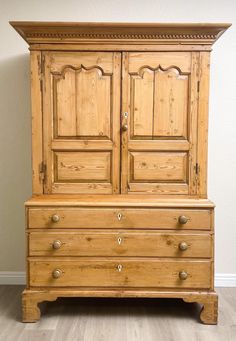 an old wooden armoire with drawers and knobs on the bottom, against a white wall